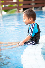 A toddler boy sitting on the edge of a swimming pool
