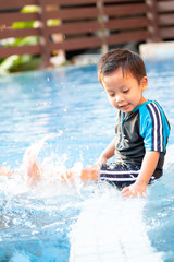Fototapeta na wymiar A toddler boy is kicking legs on the edge of a swimming pool