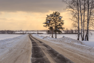 Obraz premium The road through the winter field in January evening against the sky