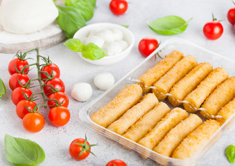 Fresh Mozzarella cheese on vintage chopping board with tomatoes and basil leaf and tray with cheese sticks on stone kitchen table background.