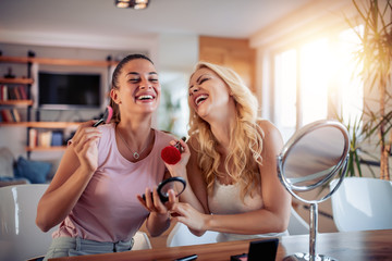 Two happy girls applying make up at home