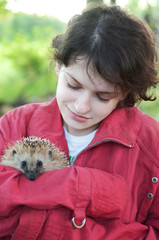 girl holds a small hedgehog in her hands and smiles