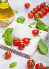 Fresh Mozzarella cheese on vintage chopping board with tomatoes and basil leaf with olive oil on stone kitchen table background.