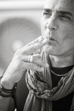 A 50y man is smoking a cigarette. Black and white. The fan coil of an air-conditioner is on the background.