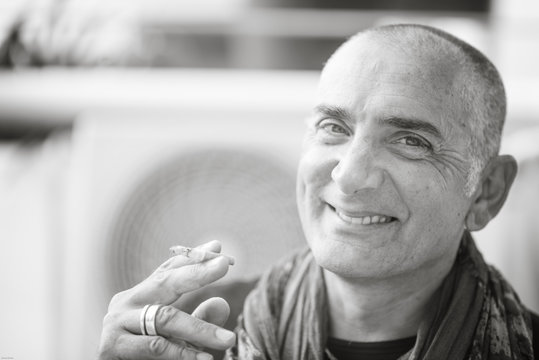 A 50y man is smoking a cigarette. Black and white. The fan coil of an air-conditioner is on the background.