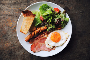 English breakfast  fried egg, ham,sausage, bacon,salad and toast on wood background in mystic light