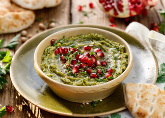Hummus. Herbal hummus with the addition of pomegranate seeds, parsley, olive oil and aromatic spices in a ceramic pot on a wooden rusty table. A healthy and delicious vegan dish, a kind of paste, dip