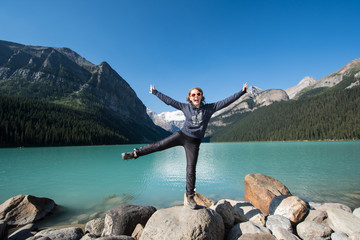 Cute young adult woman stands and balances on a pile of rocks at Lake Louise in Alberta Canada at...