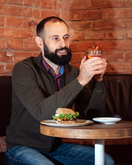 businessman male brunette beard glass hold cafe office house loft brave bearded hipster mulled wine close up hamburger