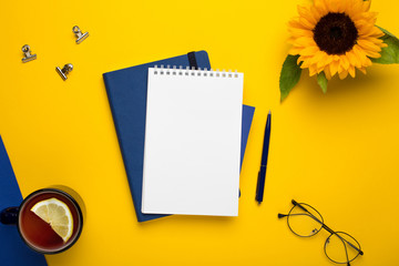 White notepad with blue notebook and pen on yellow background