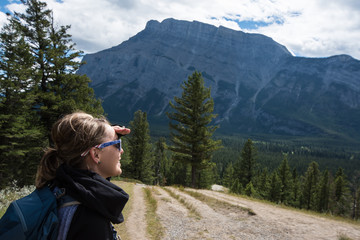 Young woman backpacker hiker looks out at the view of Banff National Park in Canada, enjoying the scenic Canadian Rockies