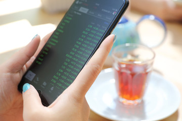 Close up on woman hand holding smartphone trading stock and data in coffee shop background business concept