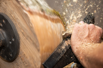 hand of man cuts piece of timber with flying sawdust and shavings