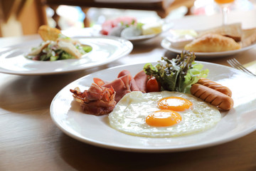Fototapeta na wymiar Breakfast set with fried eggs, bacon, sausages, beans, toasts, fresh salad and fruit on wood table