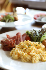 Breakfast scrambled egg with bacon sausage and salad on wood background