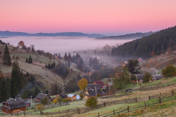 Small village in the mountains during autumn at sunrise with fog