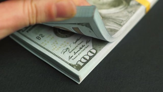 Female hand leafing through a stack of hundred dollar bills
