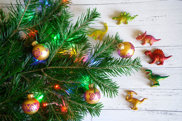 Decorated with toys and lights branch of a Christmas tree next to the figures of dinosaurs. New Year with dinosaurs