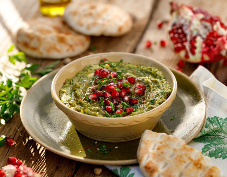 Hummus. Herbal hummus with the addition of pomegranate seeds, parsley, olive oil and aromatic spices in a ceramic pot on a wooden rusty table. A healthy and delicious vegan dish, a kind of paste, dip