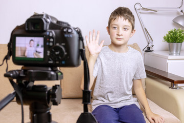 Fototapeta na wymiar A boy, male child video blogger recording vlog or podcast, streaming online. Blurred camera on tripod in front