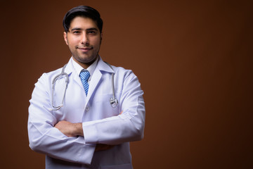 Young handsome Iranian man doctor against brown background