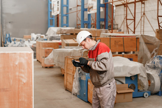 the storekeeper marks the arrival on the tablet. man driving a forklift through a warehouse in a factory. driver in uniform and protective helmet. the concept of logistics and storage