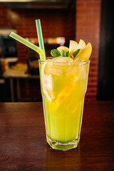 a glass of beautiful bright cocktail on a wooden surface decorated with fruits, berries, leaf of mint and basil at bar counter background