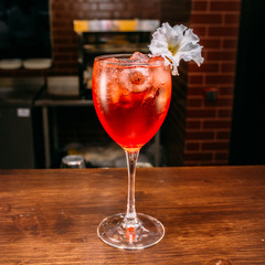 a glass of beautiful bright cocktail on a wooden surface decorated with fruits, berries, leaf of mint and basil at bar counter background