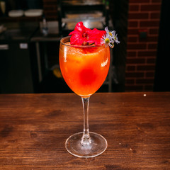 a glass of beautiful bright cocktail on a wooden surface decorated with fruits, berries, leaf of mint and basil at bar counter background