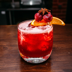 a glass of beautiful bright cocktail on a wooden surface decorated with fruits, berries, leaf of mint and basil at bar counter background