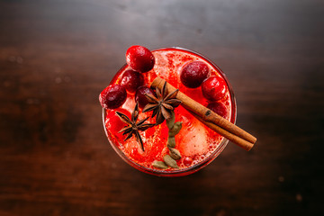 a glass of beautiful bright cocktail on a wooden surface decorated with fruits, berries, leaf of mint and basil at bar counter background