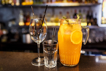 a glass of beautiful bright cocktail on a wooden surface decorated with fruits, berries, leaf of mint and basil at bar counter background