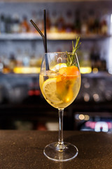 a glass of beautiful bright cocktail on a wooden surface decorated with fruits, berries, leaf of mint and basil at bar counter background
