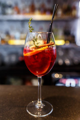 a glass of beautiful bright cocktail on a wooden surface decorated with fruits, berries, leaf of mint and basil at bar counter background