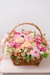flowers arrangement with various of colors in wicker basket on pink table. beautiful spring bouquet. bright room, white wall. copy space