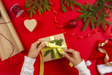 Christmas gift wrapping. Woman's hands packing Christmas present box on red table background