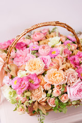 flowers arrangement with various of colors in wicker basket on pink table. beautiful spring bouquet. bright room, white wall. copy space