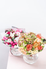 two beautiful spring bouquet. flowers arrangements with various of colors in glass vase on pink table. bright room, white wall