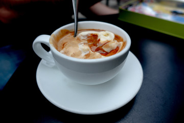 White Cup of Italian coffee-based dessert Affogato coffee with dessert spoon in table. Form of a scoop of vanilla gelato or ice cream topped or drowned with a shot of hot espresso. 