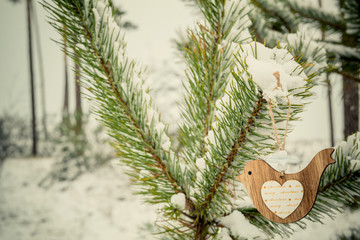 Wooden bird decoration on branch of pine among the winter forest. Christmas and happy New year concept