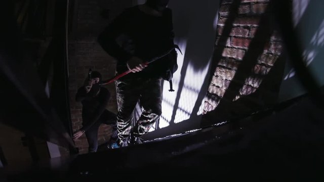 Gang of two robbers with gun and scrap climbing stairs. Dangerous bandits getting into apartment for commit crime. Indoors. Darkness.
