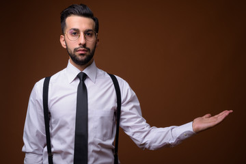 Young handsome bearded Iranian businessman against brown backgro