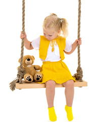A little girl is swinging on a swing with a teddy bear.