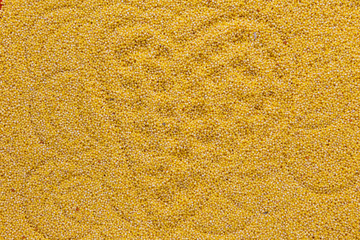 Yellow dry uncooked millet background with heart shape on it, top view, vertical