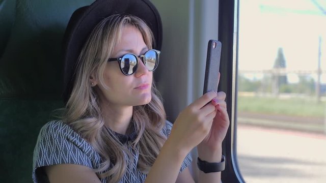 Caucasian girl in a hat travels in a train. Takes photos of nature on a mobile smartphone. Slow Motion. Close up