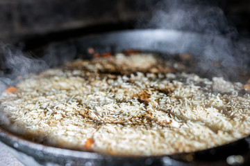 cooking Rice for pilaw or paella in iron cauldron over open fire. Smoke and steam. Tasty food preparing outdoor process background