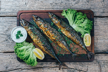 A deliciously roasted mackerel on a grill, presented on a wooden board, and along the leaves of...