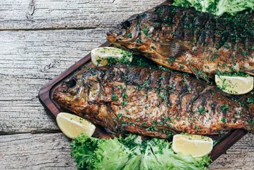 Photo sur Plexiglas Grill / Barbecue A deliciously roasted carp on a grill, presented on a wooden board, and along the leaves of green salad and pieces of lemon