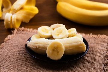 White flesh of ripe banana sliced into pieces in a plate, linen cloth napkin on wooden background.