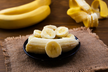 Ripe banana cut into pieces in a porcelain plate, linen napkin, wooden background.
